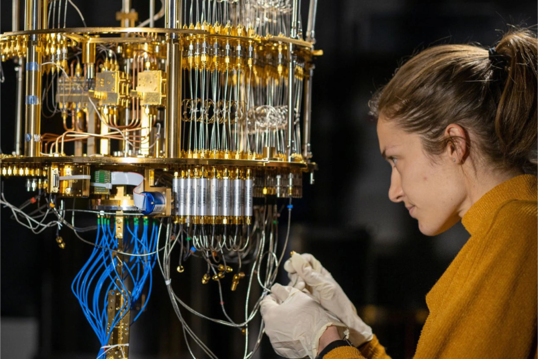 A person works on a complex, golden device, possibly a quantum computer, with many cables and connectors.